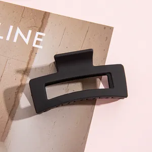 Primer plano de una pinza para el pelo rectangular negra mate sobre un fondo rosa suave