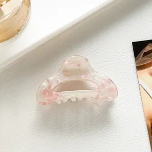 Dettaglio della piccola molletta in acetato con motivo floreale rosa su base bianco crema