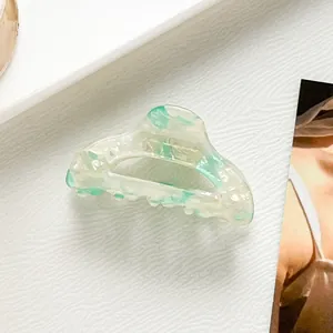 Dettaglio di una piccola molletta per capelli in acetato con motivo marmorizzato verde