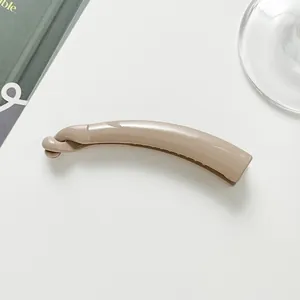 Close-up of a small glossy light brown plastic banana hair clip on white desk background