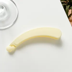 Close-up of a matte cream yellow banana hair clip on a minimalist white surface