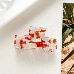 Dettaglio molletta per capelli in acetato crema con motivo marmorizzato rosso e denti