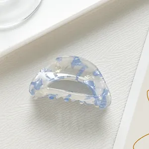 Macro view of semi-circular acetate hair claw with blue floral patterns and pearly finish