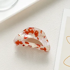 Detailed view of semi-circular acetate hair claw with orange floral patterns