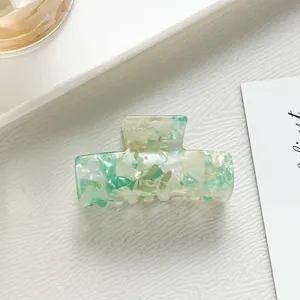 Dettaglio molletta per capelli in acetato verde menta su superficie minimalista