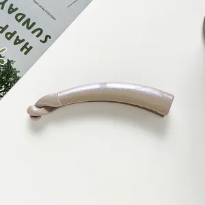 Detailed view of the pearlescent champagne banana hair clip on a minimalist surface