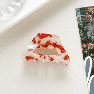 Vue détaillée de la pince à cheveux en acétate marbré rouge et blanc sur plateau