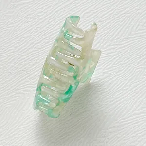 Dettaglio della pinza per capelli in acetato marmorizzato verde e bianco su tessuto