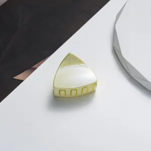 Close-up of a small triangular hair claw clip with glitter finish in pale yellow resin