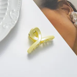 Vue détaillée d'une pince à cheveux jaune pâle pailletée avec une finition nacrée torsadée
