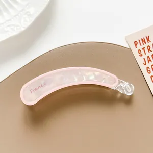 Detalle de una pinza banana rosa y perlada con el texto France sobre fondo decorativo
