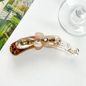 Détail d'une pince banane en résine ambrée avec fleur rose et strass marron sur le dessus
