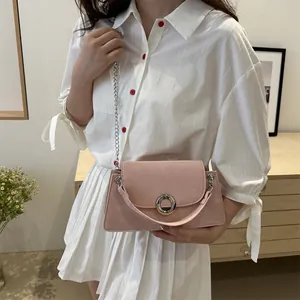 Sac bandoulière rose en daim avec chaîne argentée, porté par un mannequin en tenue élégante