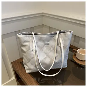 Grand sac cabas matelassé gris clair avec fines anses et logo sur table en bois
