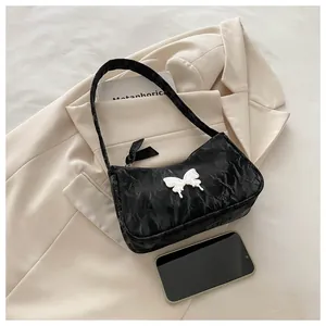 Detail of black pleated hobo bag featuring a large white butterfly ornament on the front