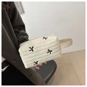 Detail of cream quilted makeup bag with bow embroidery and ribbon handle held by hand
