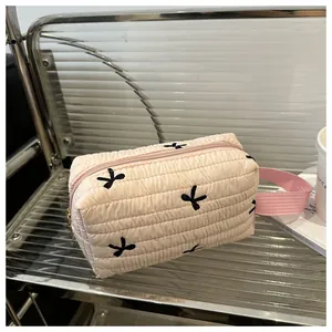 Close-up of a pink quilted cosmetic bag with black embroidery on a modern shelf