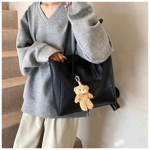Classic black oversized tote bag with plush bear charm worn on shoulder