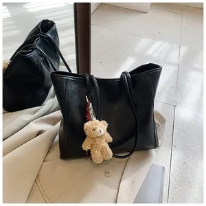 Detail of black matte PU leather tote bag with long straps and a plush bear charm
