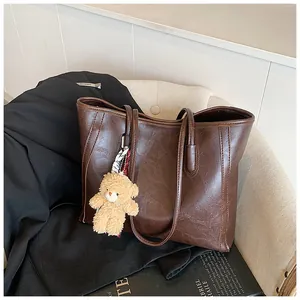 Detailed texture of dark brown faux leather tote bag with plush bear charm on chair