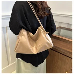 Detail of apricot pleated tote bag with letter embossing worn by a model in interior setting