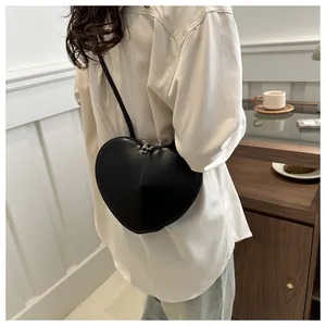 Detailopname van een hartvormige zwarte crossbodytas gedragen met een wit overhemd