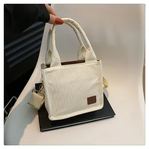 Detail der cremeweißen Mini-Tote-Bag aus Cord mit Streifenstruktur und Lederaufnäher