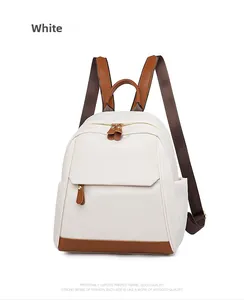 Close-up of white Oxford fabric backpack with brown leather trim and golden zippers
