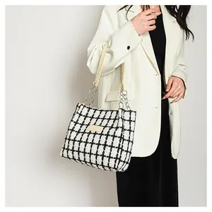 Detail of black and white tweed tote bag with metal chain strap and leather patch