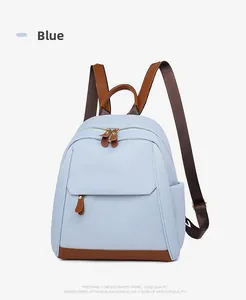 Detail of light blue oxford backpack featuring brown leather straps and gold metal zippers