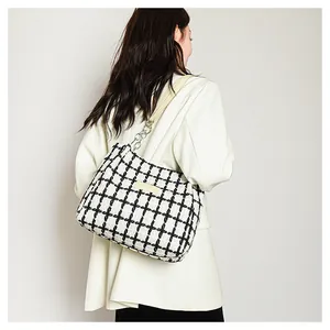 Detail of checkered tweed tote bag with metal chain strap worn by a model in a beige coat