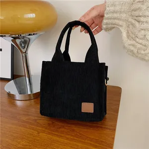 Schicke schwarze Mini-Tragetasche aus Cord mit braunem Lederpatch auf Holztisch