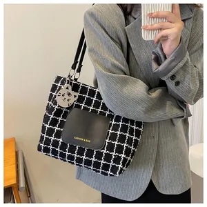 Détail d'un sac cabas à carreaux avec poche en cuir et breloque chat en métal