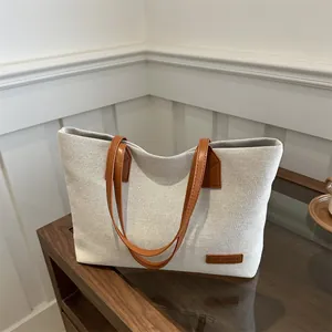 Minimalist canvas tote bag with brown leather handles and fashion tag on wooden cabinet
