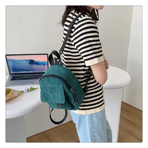 Detalle de una mini mochila de pana verde oscuro usada por modelo en un entorno moderno