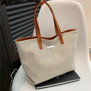 Large beige canvas tote bag with brown leather handles and silver metal detail