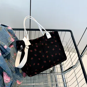 Black corduroy tote bag with strawberry prints and white straps in a shopping cart