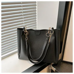 Detail of black pebbled leather tote bag with elegant gold chain shoulder strap