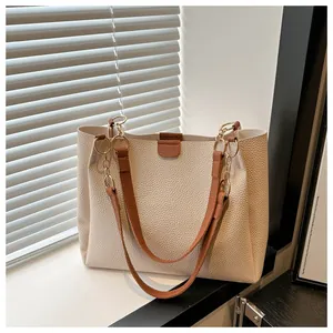 Macro view of beige lychee textured leather tote bag with brown contrast strap detail