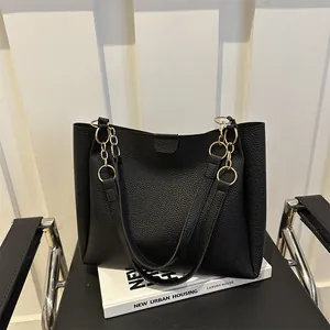 Black pebbled leather tote bag with large capacity and gold chain handle on a chair