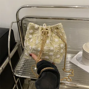 Beige straw bucket bag with floral embroidery and gold chain strap in minimalist setting
