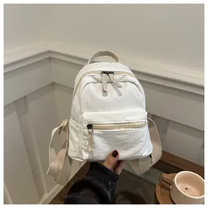 Close-up of a mini white canvas backpack held by hand in a minimalist setting