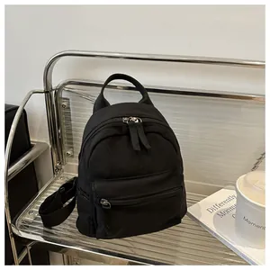 Close-up of a black canvas mini backpack with dual zippers on a modern metal display shelf