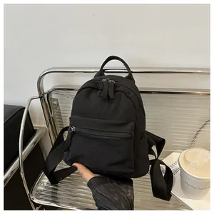 Mini black canvas backpack shown on a chair next to a coffee cup for lifestyle size reference