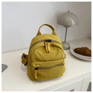 Close-up of a mini mustard yellow canvas backpack with zipper pocket on a white table