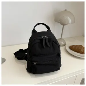 Detail of a black canvas mini backpack featuring durable zippers and a stylish side strap