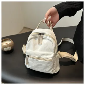 Handheld view of a mini white canvas backpack with zip pockets and adjustable straps