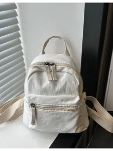 Minimalist off-white canvas mini backpack with dual zippers shown in natural window light