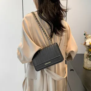 Sac à bandoulière noir chic avec sangle chaîne porté sur un trench-coat beige