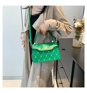 Detail of bright green quilted handbag with golden heart embroidery and chain trim